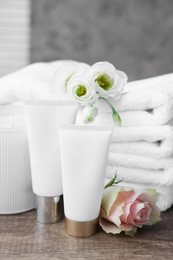 Photo of Cosmetic products, scented candle and folded towels with flowers on wooden table indoors