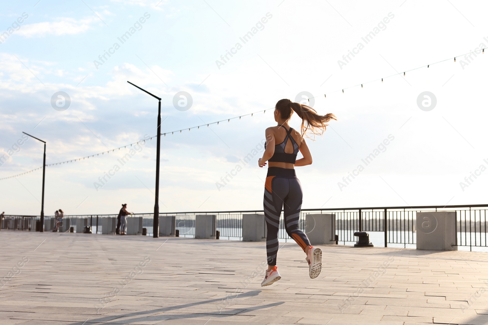 Photo of Young woman running on pier near river in morning. Space for text