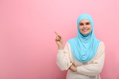 Photo of Portrait of Muslim woman in hijab pointing at something on pink background, space for text