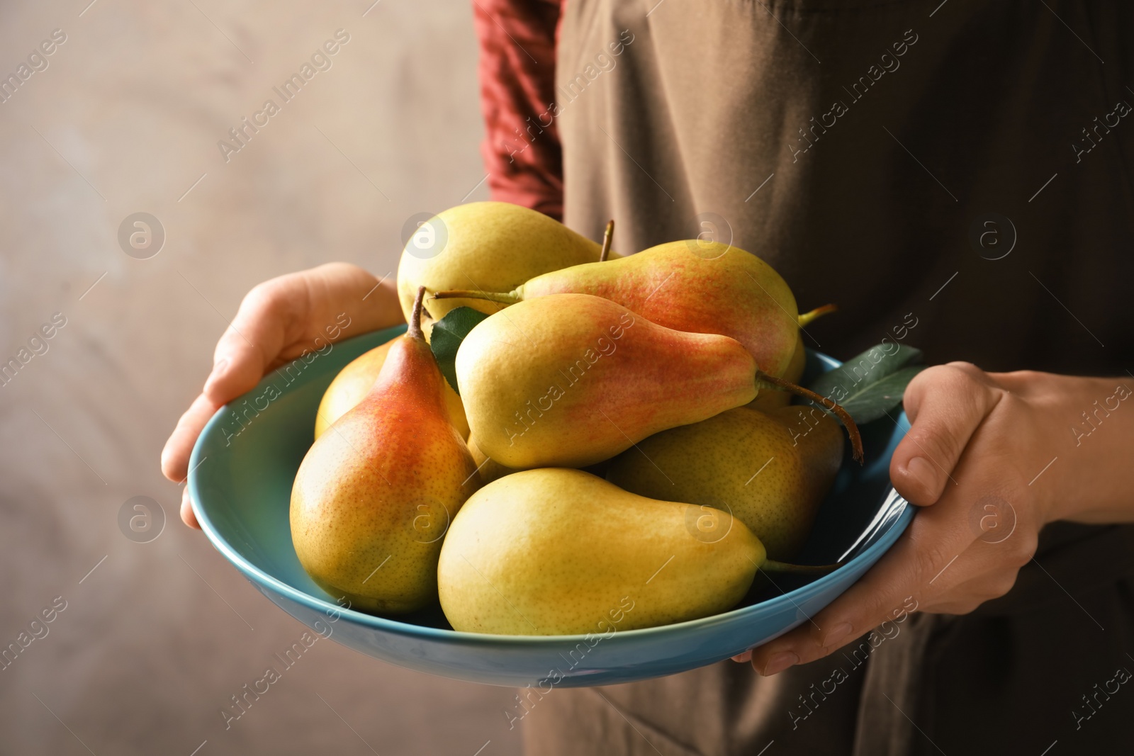 Photo of Woman holding plate with ripe pears on grey background, closeup