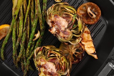 Photo of Tasty grilled artichoke and asparagus on pan, top view