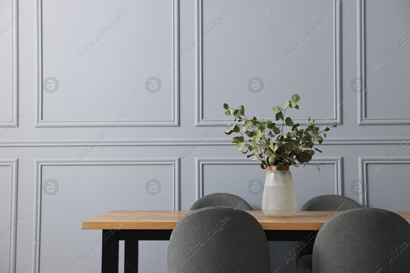 Photo of Soft chairs, table and vase with eucalyptus branches in stylish dining room. Space for text