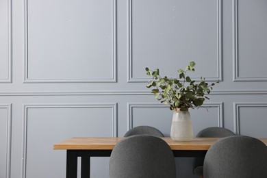 Soft chairs, table and vase with eucalyptus branches in stylish dining room. Space for text