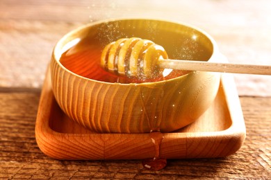 Image of Natural honey in wooden bowl and dipper on table under sunlight, closeup