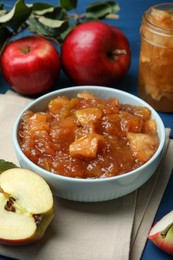 Photo of Tasty apple jam in bowl and fresh fruits on blue table