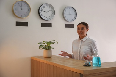 Photo of Receptionist at countertop with antiseptic gel and service bell in hotel
