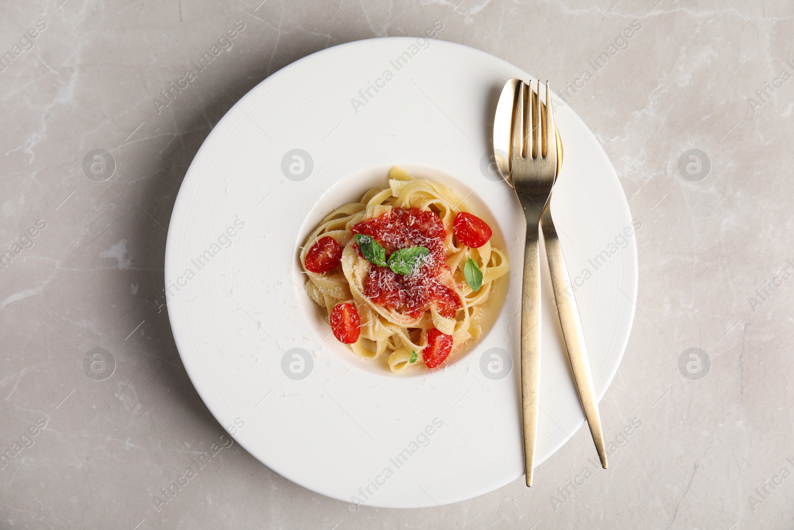 Photo of Tasty pasta with tomatoes, cheese and basil on light grey marble table, top view