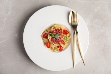 Tasty pasta with tomatoes, cheese and basil on light grey marble table, top view