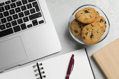 Photo of Chocolate chip cookies, laptop and notebook on light gray table in office, flat lay