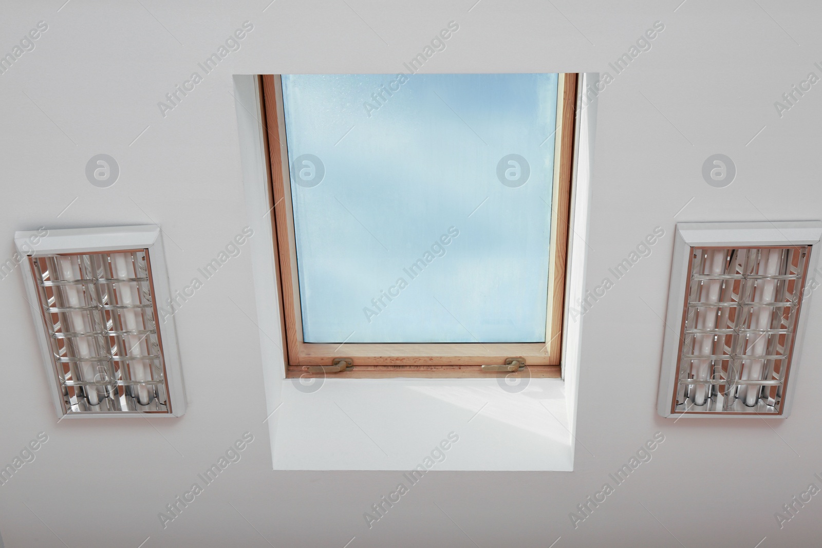 Photo of Skylight roof window and lamps on slanted ceiling in attic room, bottom view