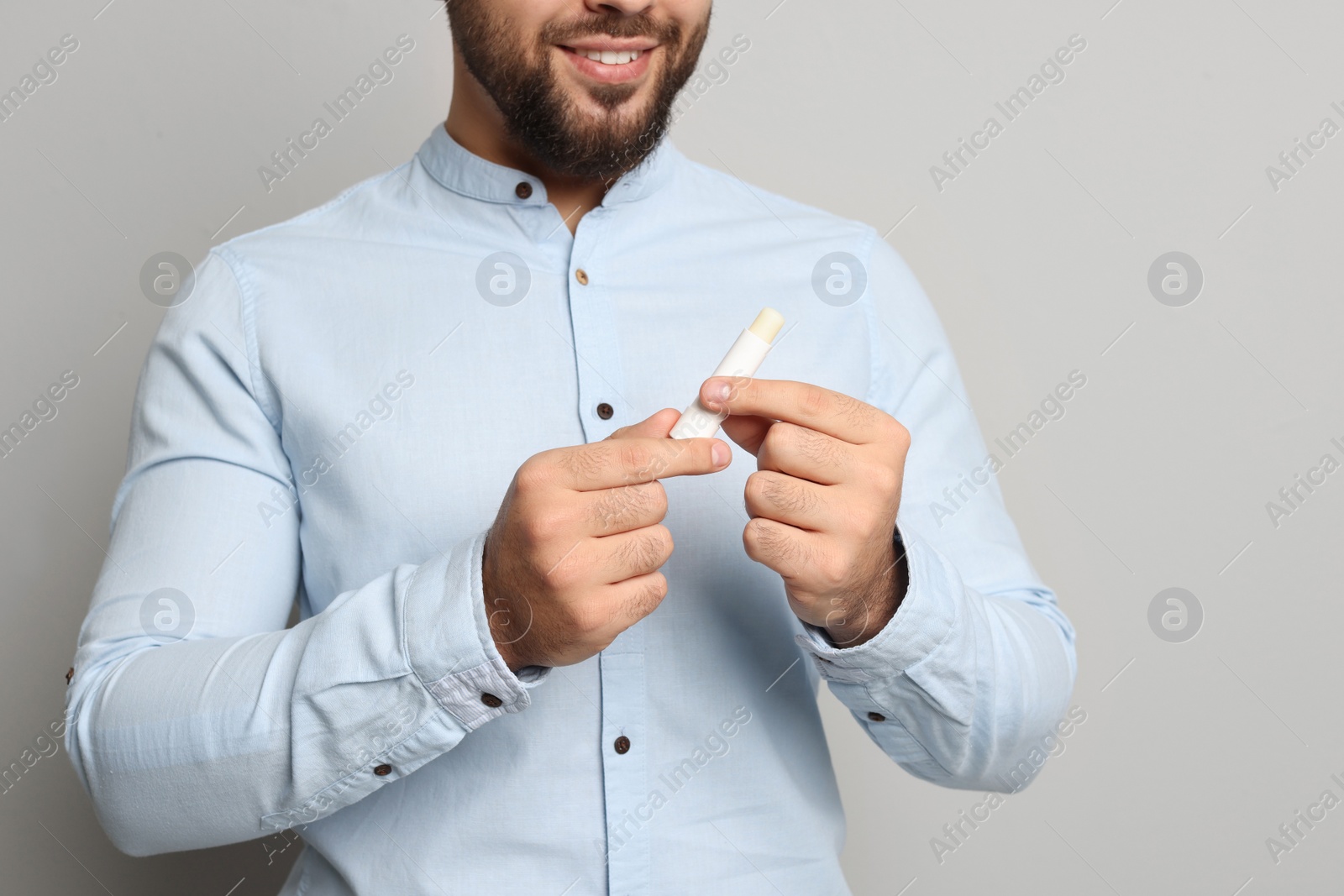 Photo of Young man with lip balm on grey background, closeup