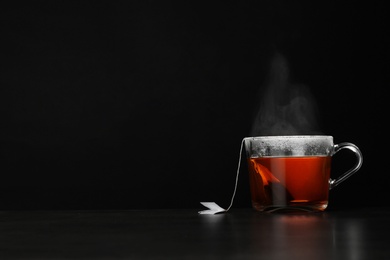 Photo of Glass cup of hot tea on table against black background, space for text