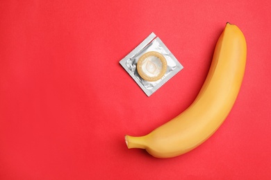 Condom with banana and space for text on red background, flat lay. Safe sex