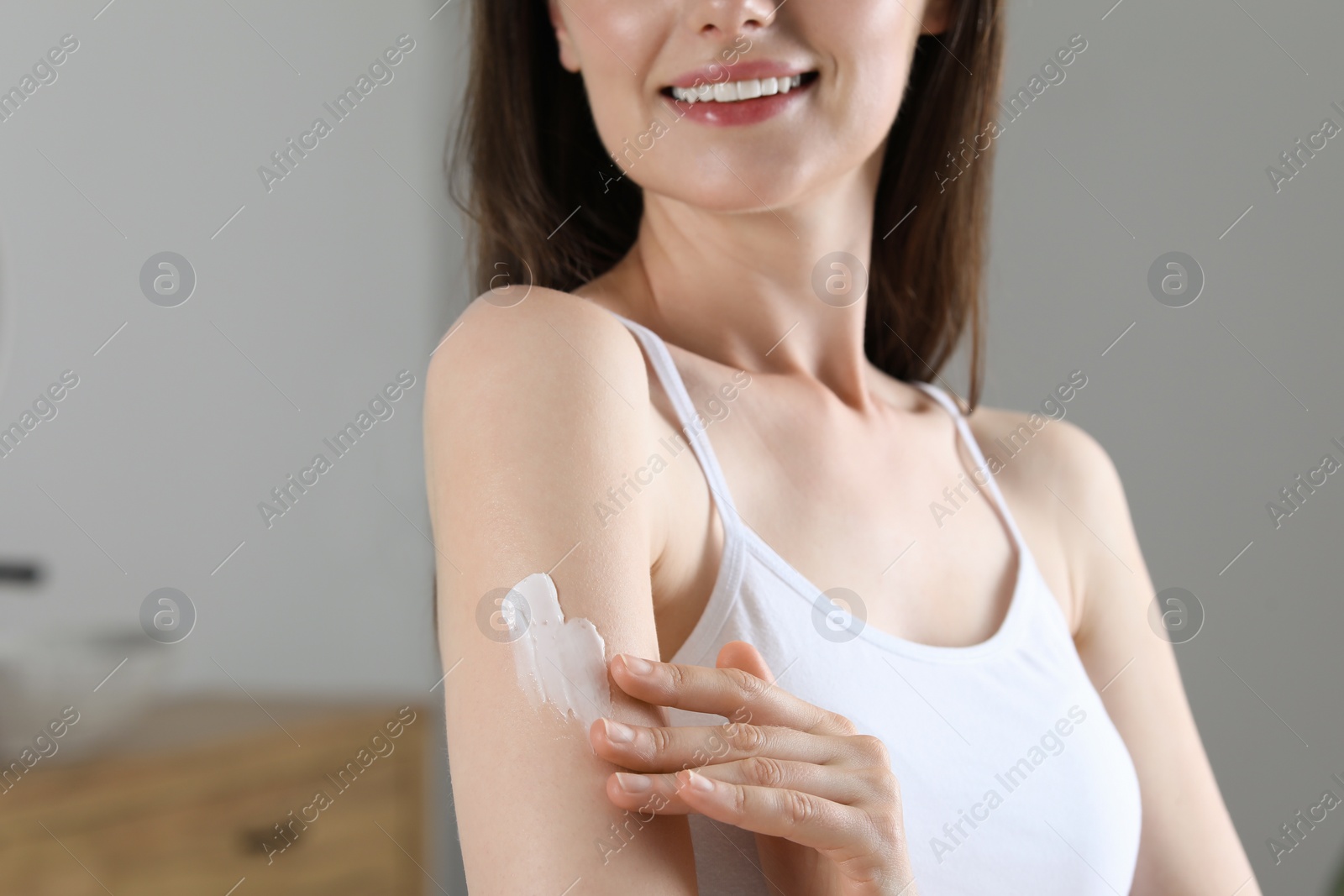 Photo of Woman applying body cream onto arm indoors, closeup. Space for text