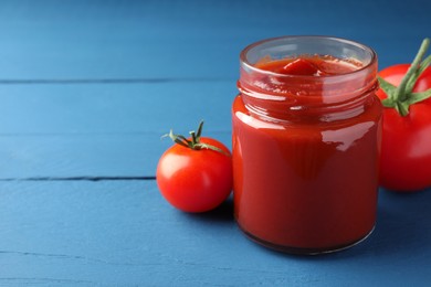 Photo of Jar of tasty ketchup and tomatoes on blue wooden table, closeup. Space for text