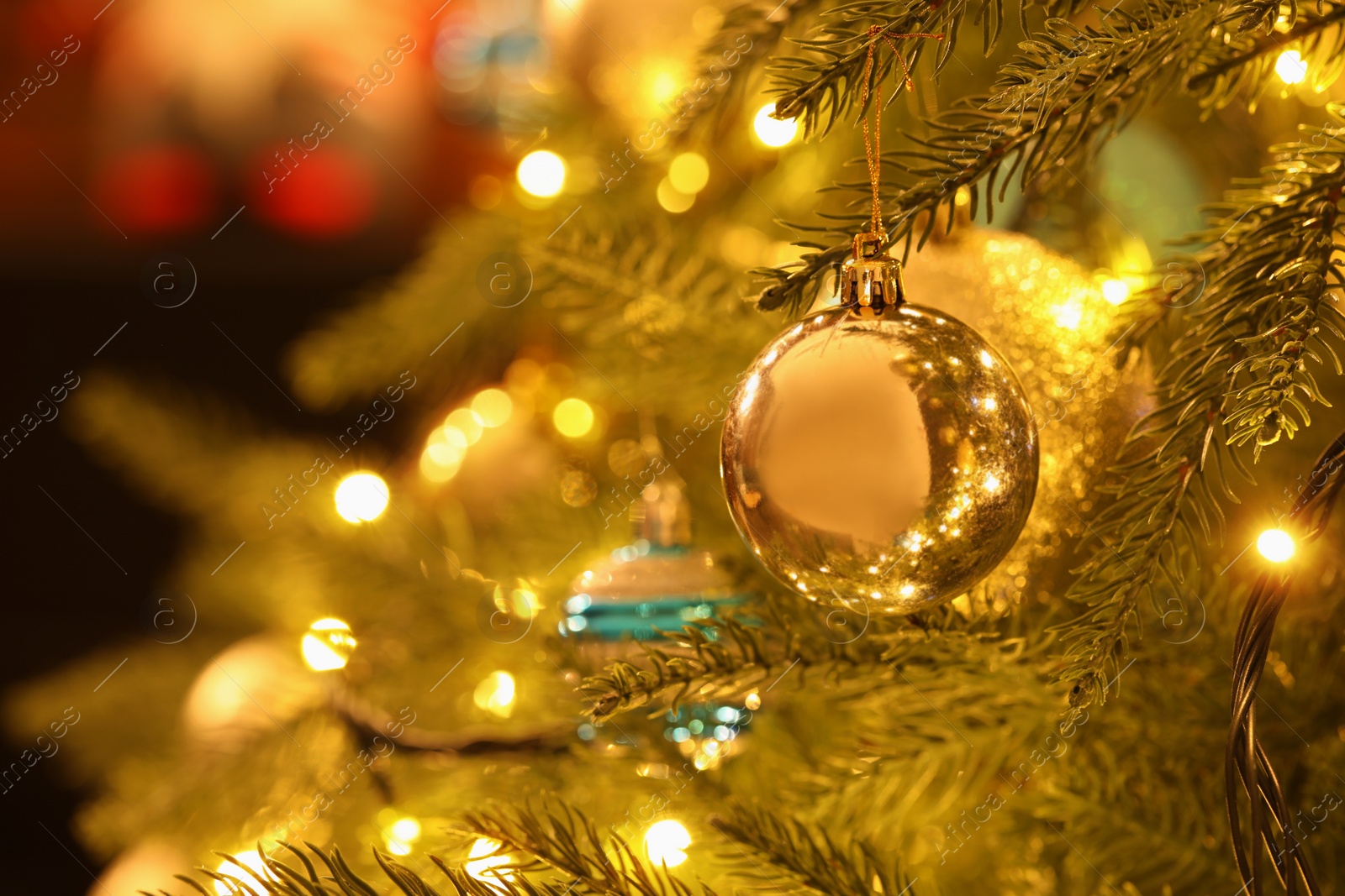 Photo of Beautiful golden Christmas ball hanging on fir tree branch against blurred background, closeup. Space for text