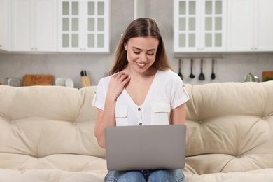 Happy woman with laptop on couch in room