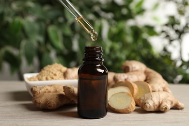 Photo of Dripping ginger essential oil from pipette into bottle on wooden table