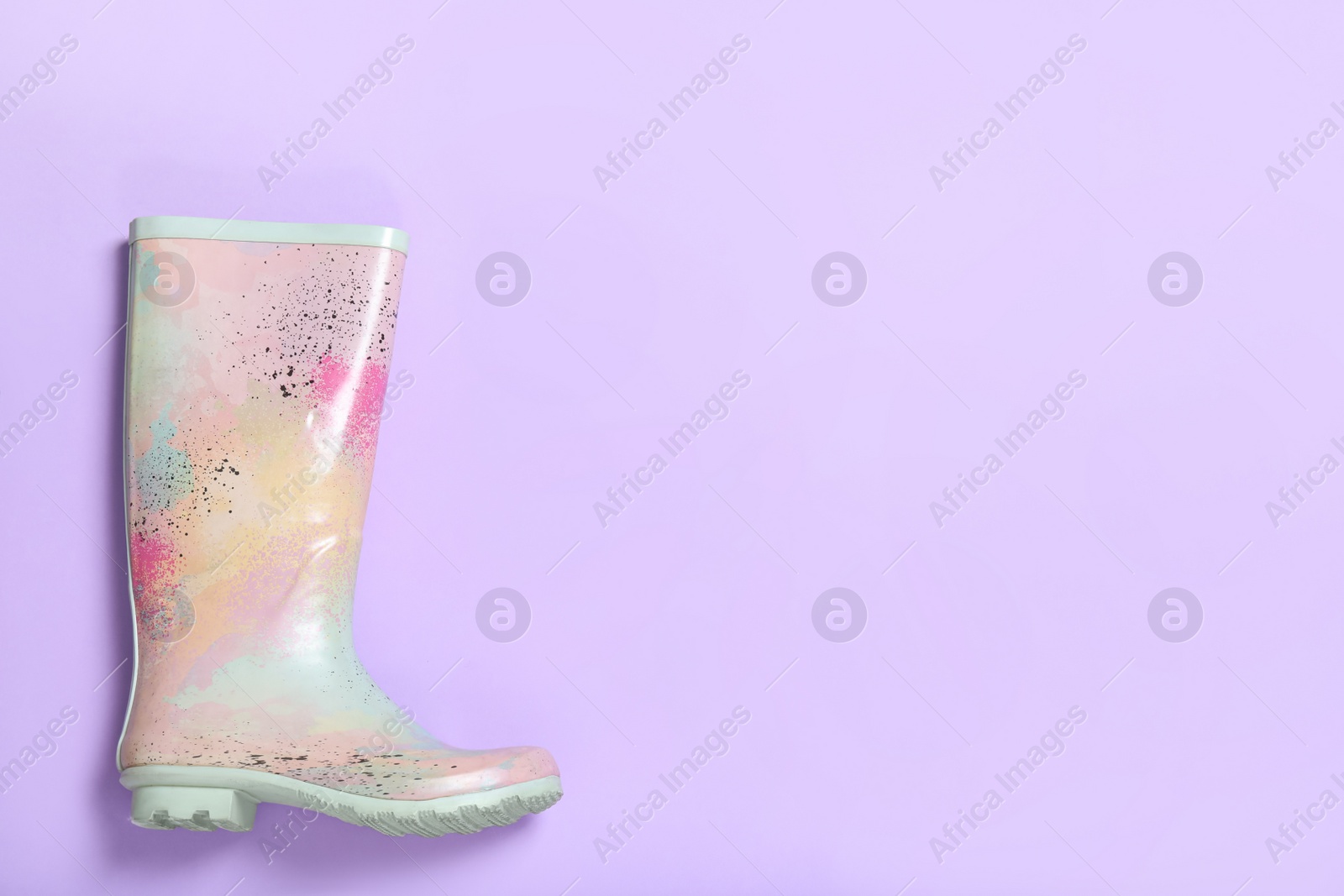 Photo of Colorful rubber boot on violet background, top view. Space for text