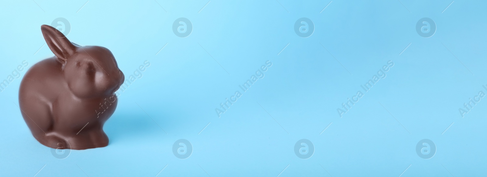 Photo of Chocolate Easter bunny on light blue background, space for text