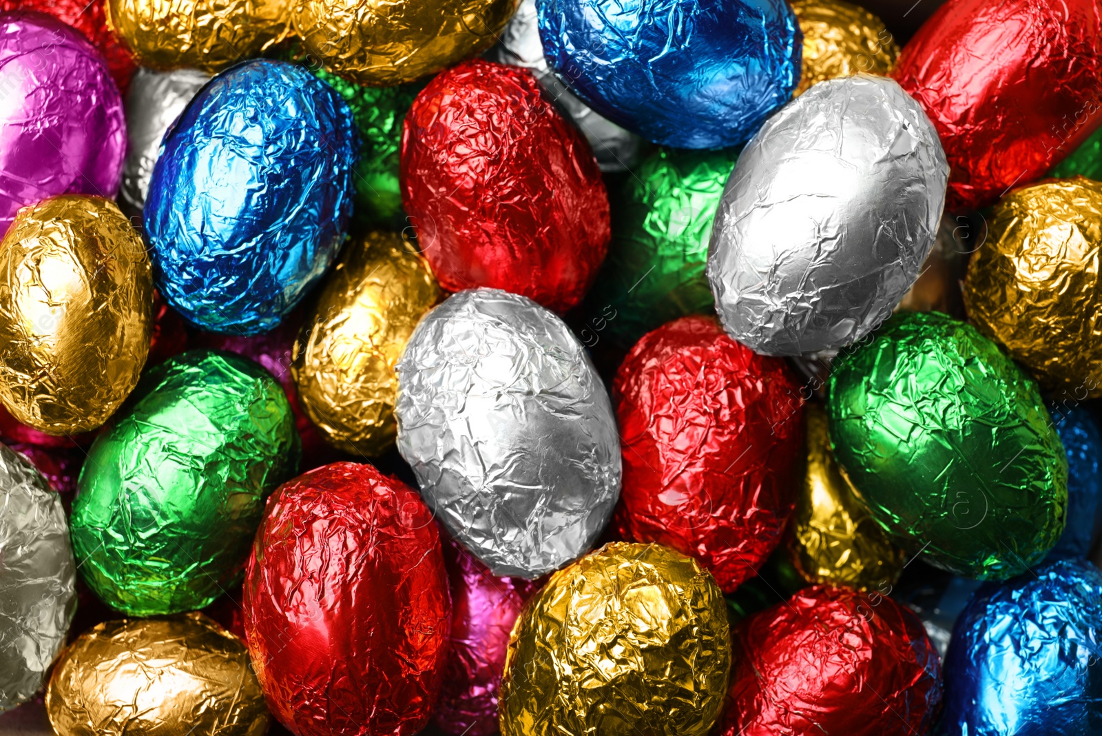 Photo of Chocolate eggs wrapped in colorful foil as background, top view