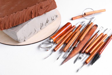 Photo of Clay and set of crafting tools on white textured table, closeup