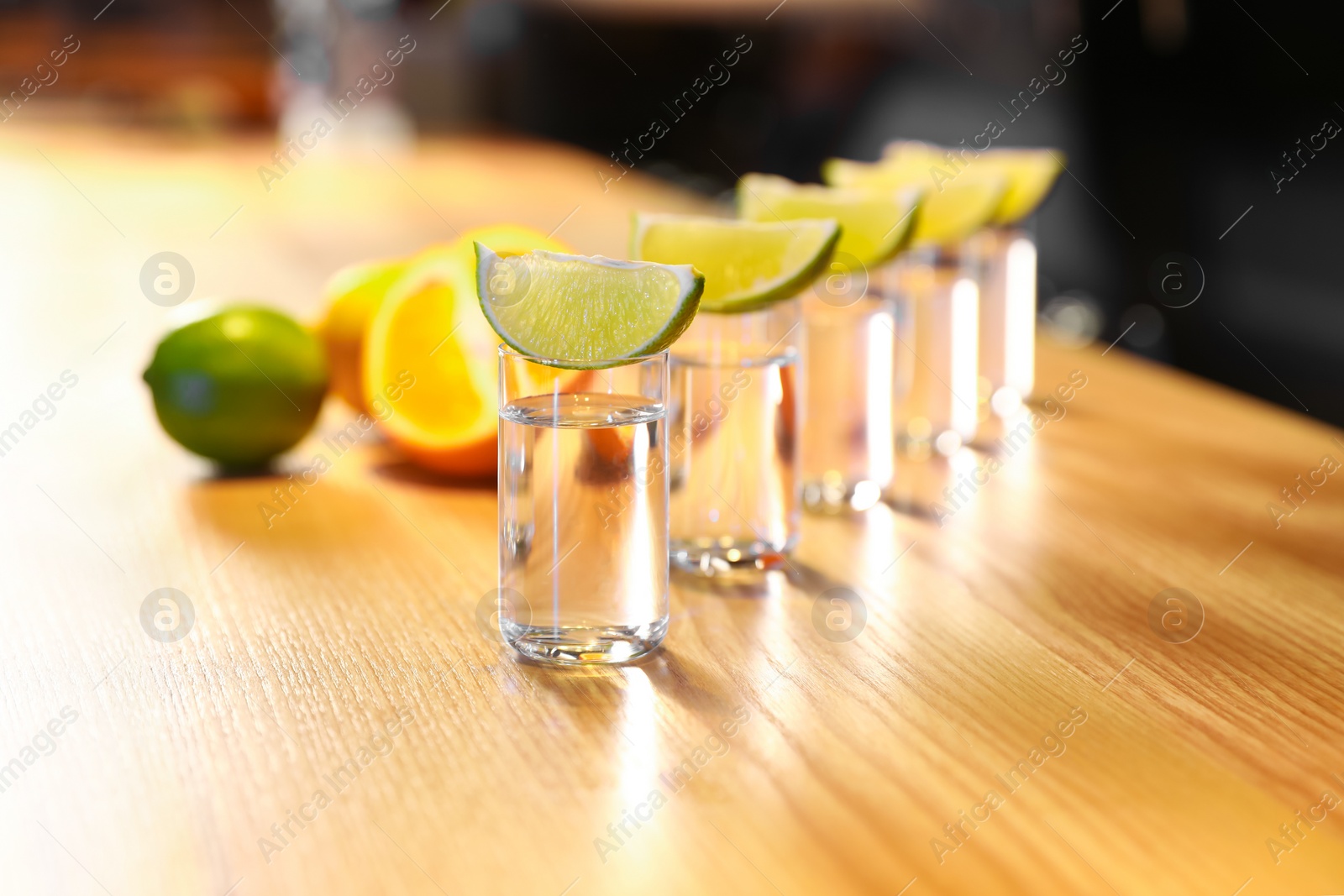 Photo of Vodka shots and lime slices on wooden bar counter