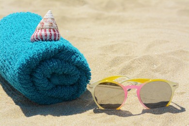Towel with stylish sunglasses and seashell on sand outdoors, closeup. Beach accessories