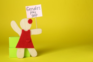 Gender pay gap. Wooden figure of woman with sign on yellow background, space for text
