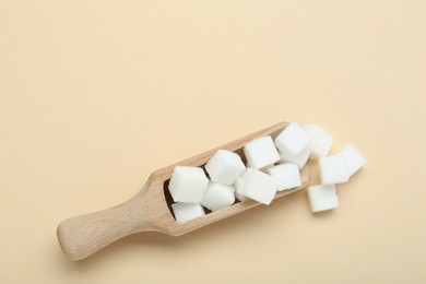 White sugar cubes and wooden scoop on beige background, top view. Space for text