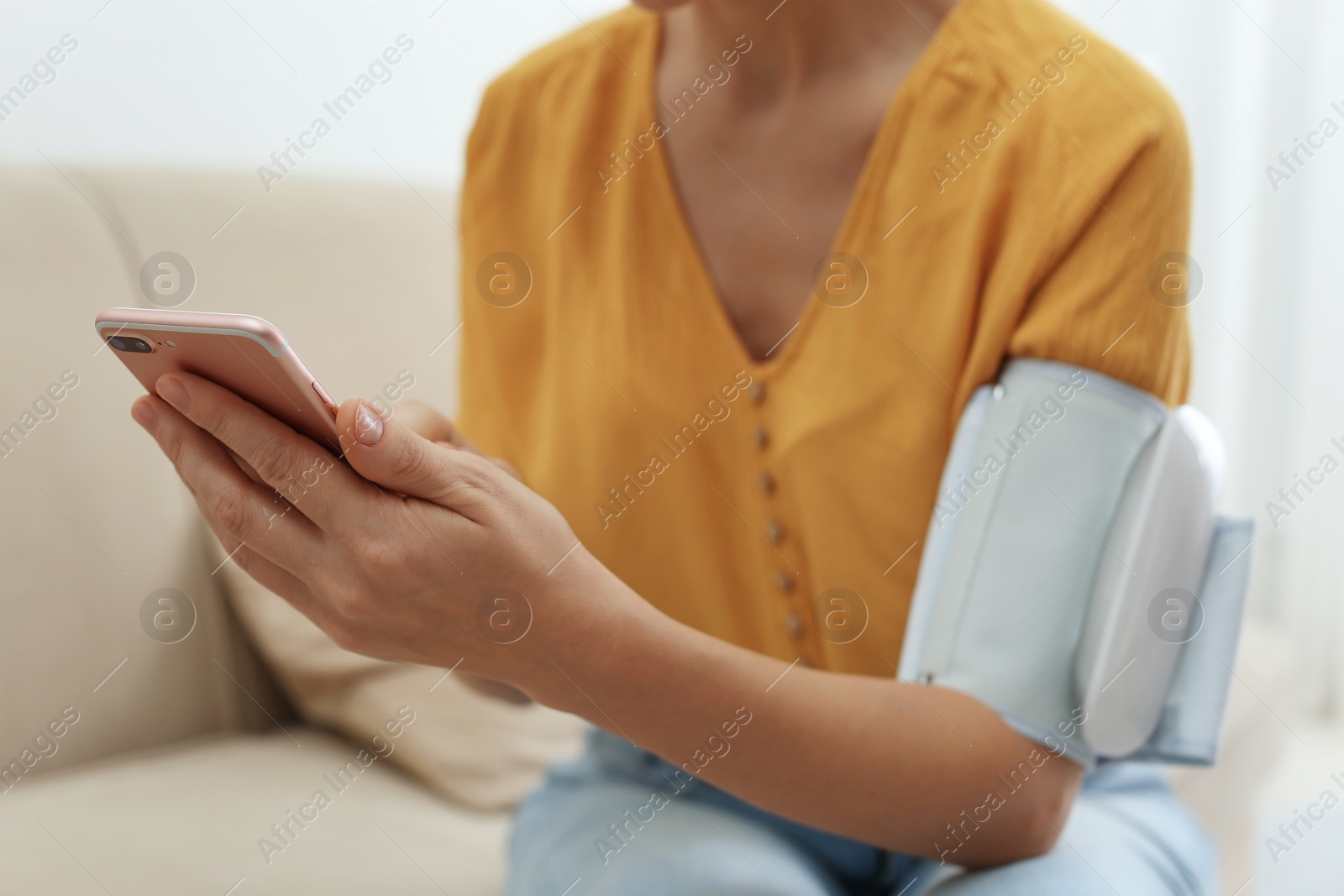 Photo of Woman checking blood pressure with modern monitor and smartphone indoors, closeup. Cardiology concept