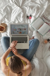 Photo of Woman and laptop with open cooking blog on bed, top view