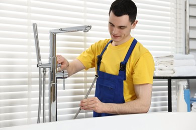 Photo of Young plumber repairing metal faucet in bathroom
