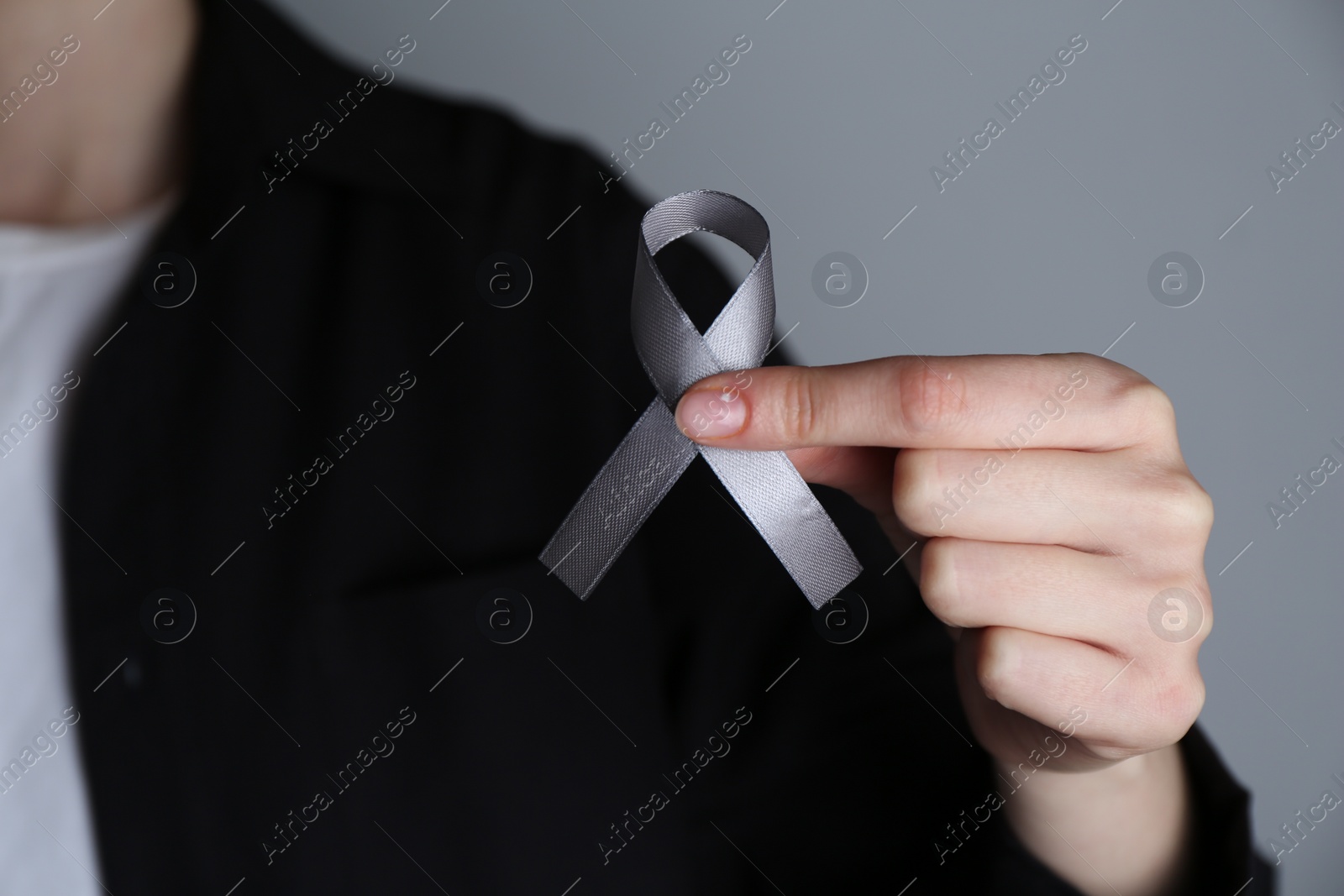 Photo of Woman holding grey awareness ribbon on color background, closeup