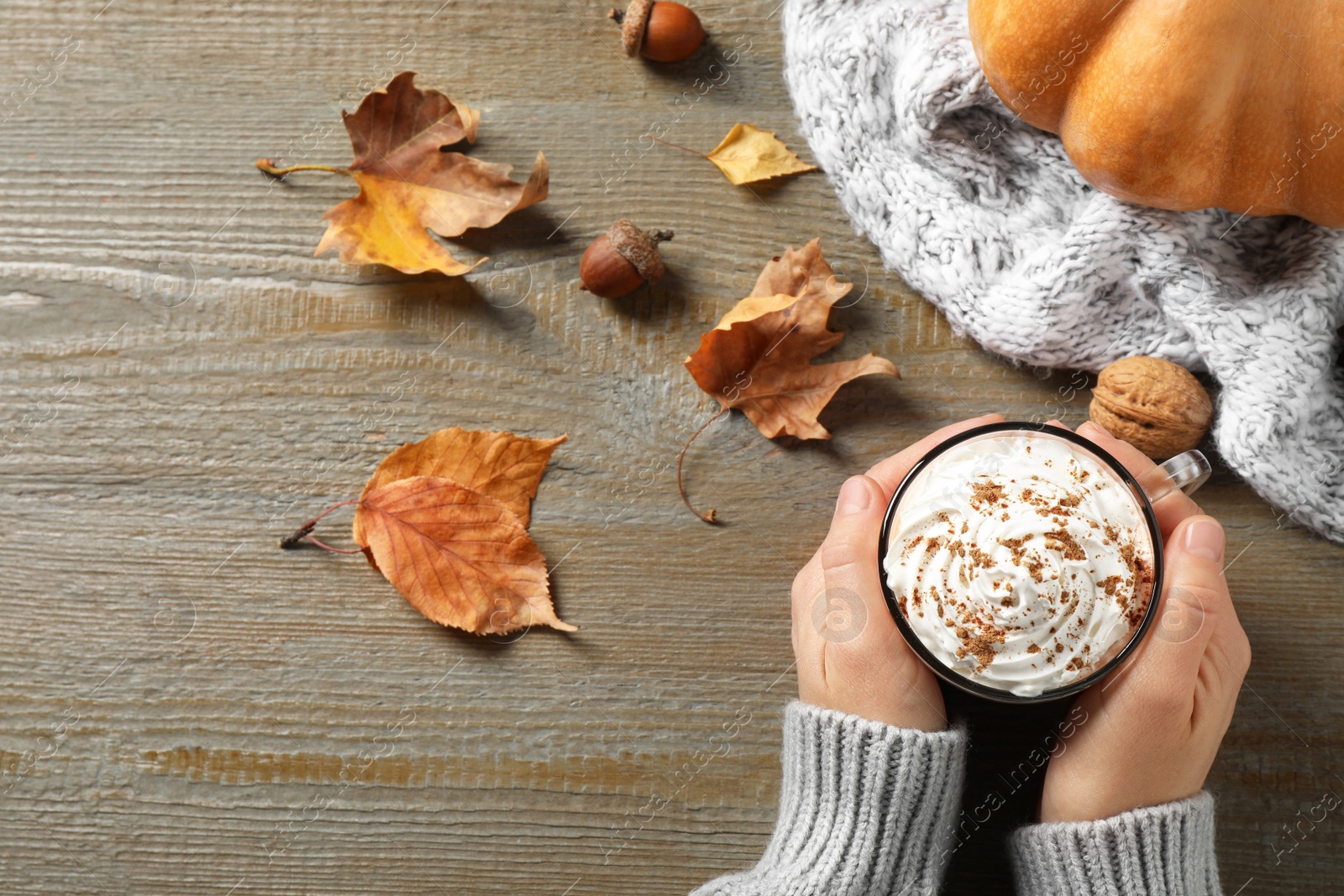 Photo of Woman with cup of pumpkin spice latte at wooden table, top view