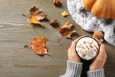 Photo of Woman with cup of pumpkin spice latte at wooden table, top view