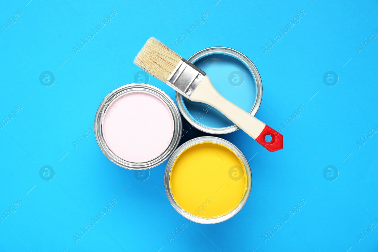 Photo of Cans of colorful paints and brush on light blue background, flat lay