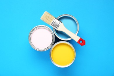 Photo of Cans of colorful paints and brush on light blue background, flat lay