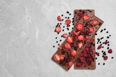 Photo of Chocolate bars with freeze dried berries on grey marble table, flat lay Space for text