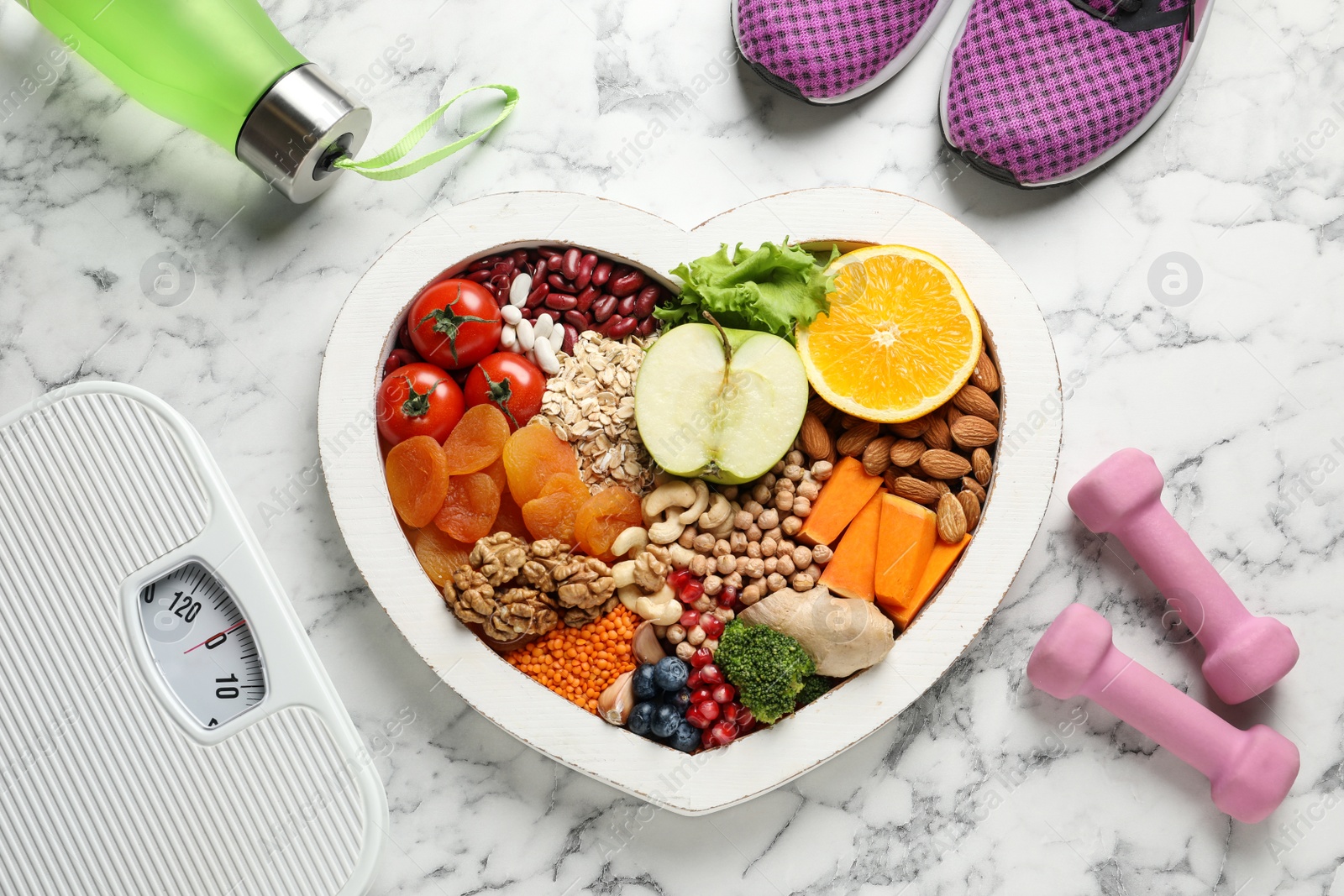 Photo of Heart shaped tray with healthy products and sports equipment on marble background, flat lay