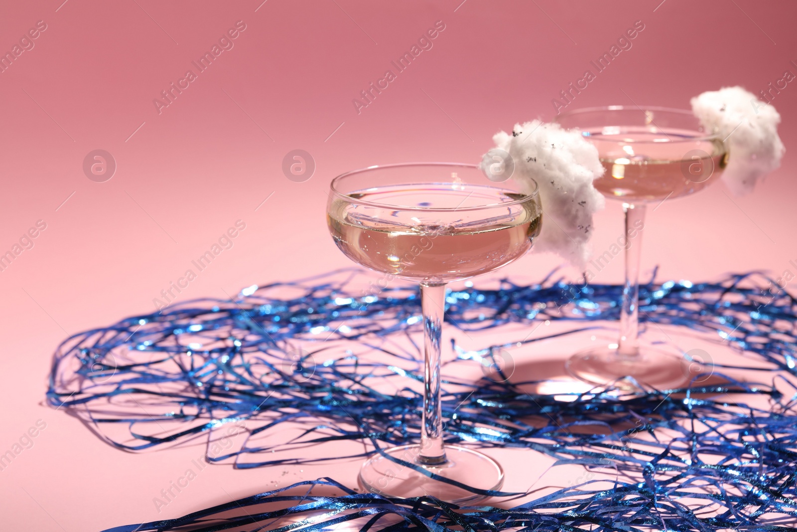 Photo of Tasty cocktail in glasses decorated with cotton candy and blue shiny streamers on pink background, space for text