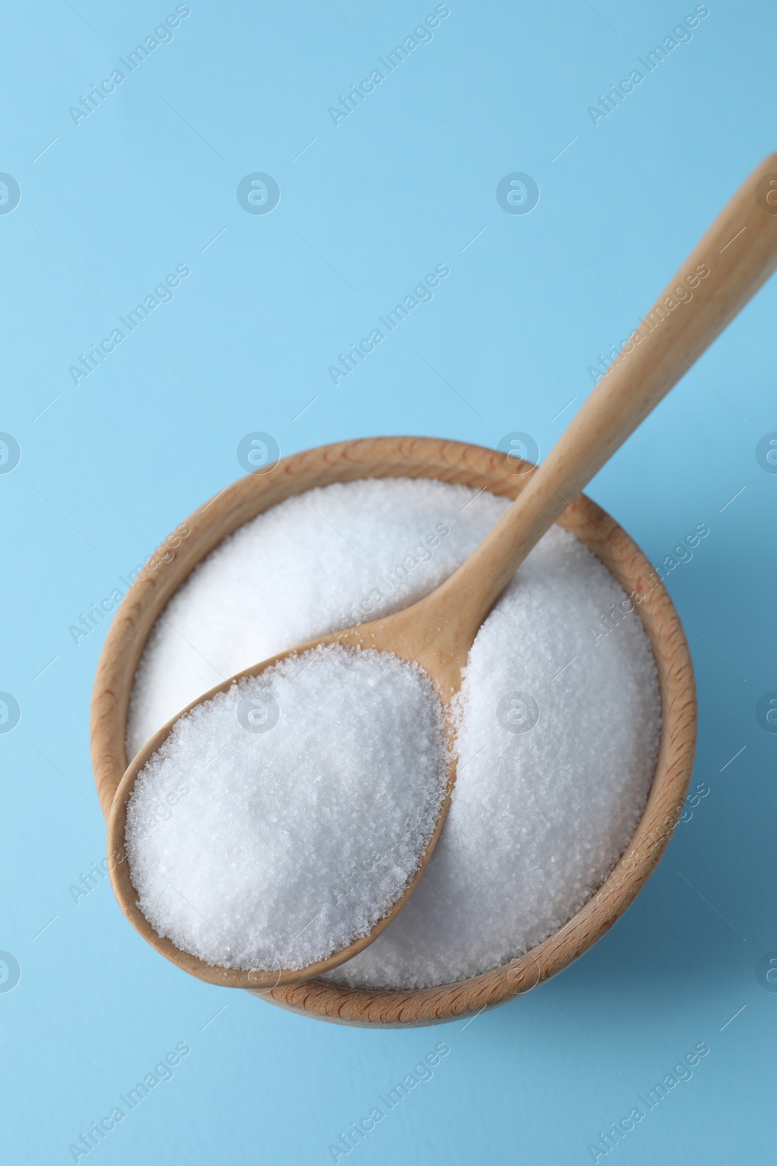 Photo of Organic white salt in bowl and spoon on light blue background, top view