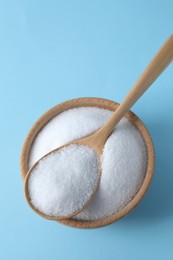 Photo of Organic white salt in bowl and spoon on light blue background, top view