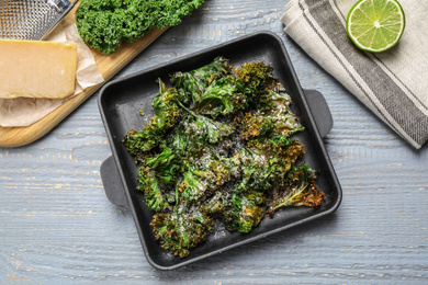 Photo of Tasty baked kale chips on light grey wooden table, flat lay