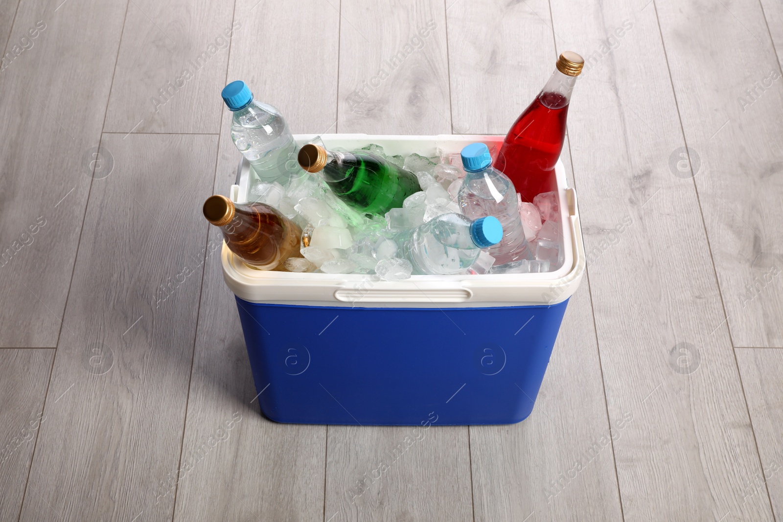 Photo of Blue plastic cool box with ice cubes and refreshing drinks on wooden floor