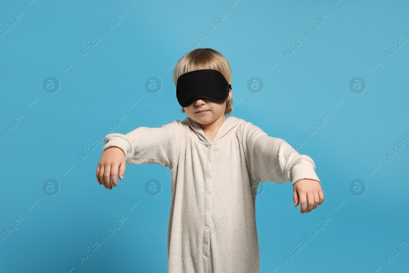 Photo of Boy in pajamas and sleep mask sleepwalking on light blue background