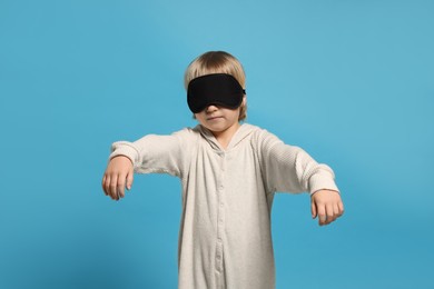 Photo of Boy in pajamas and sleep mask sleepwalking on light blue background