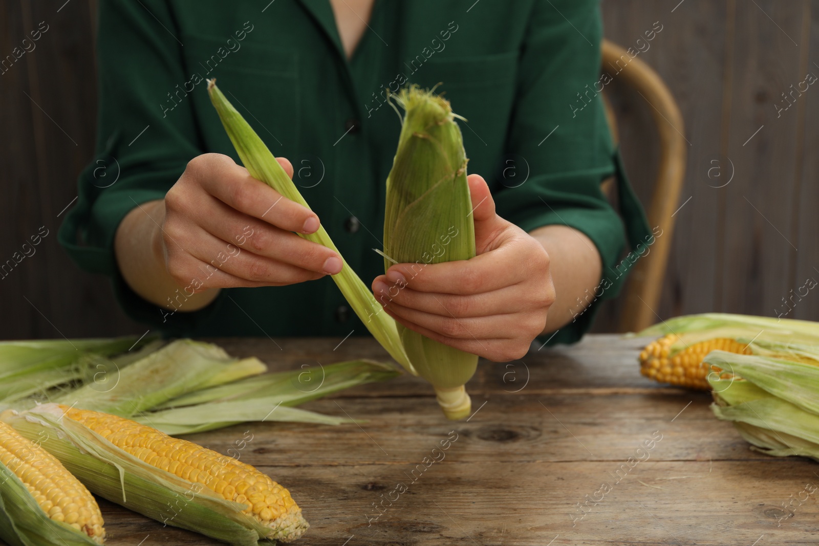 Photo of Woman husking corn cob at wooden table, closeup