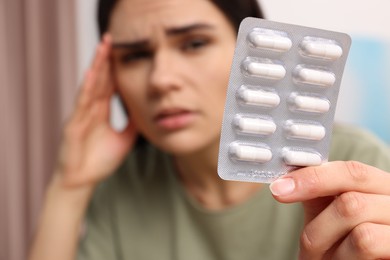 Photo of Sad woman with blister of pills suffering from headache indoors, selective focus