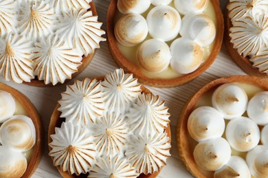 Photo of Many different tartlets with meringue on white wooden table, flat lay. Tasty dessert